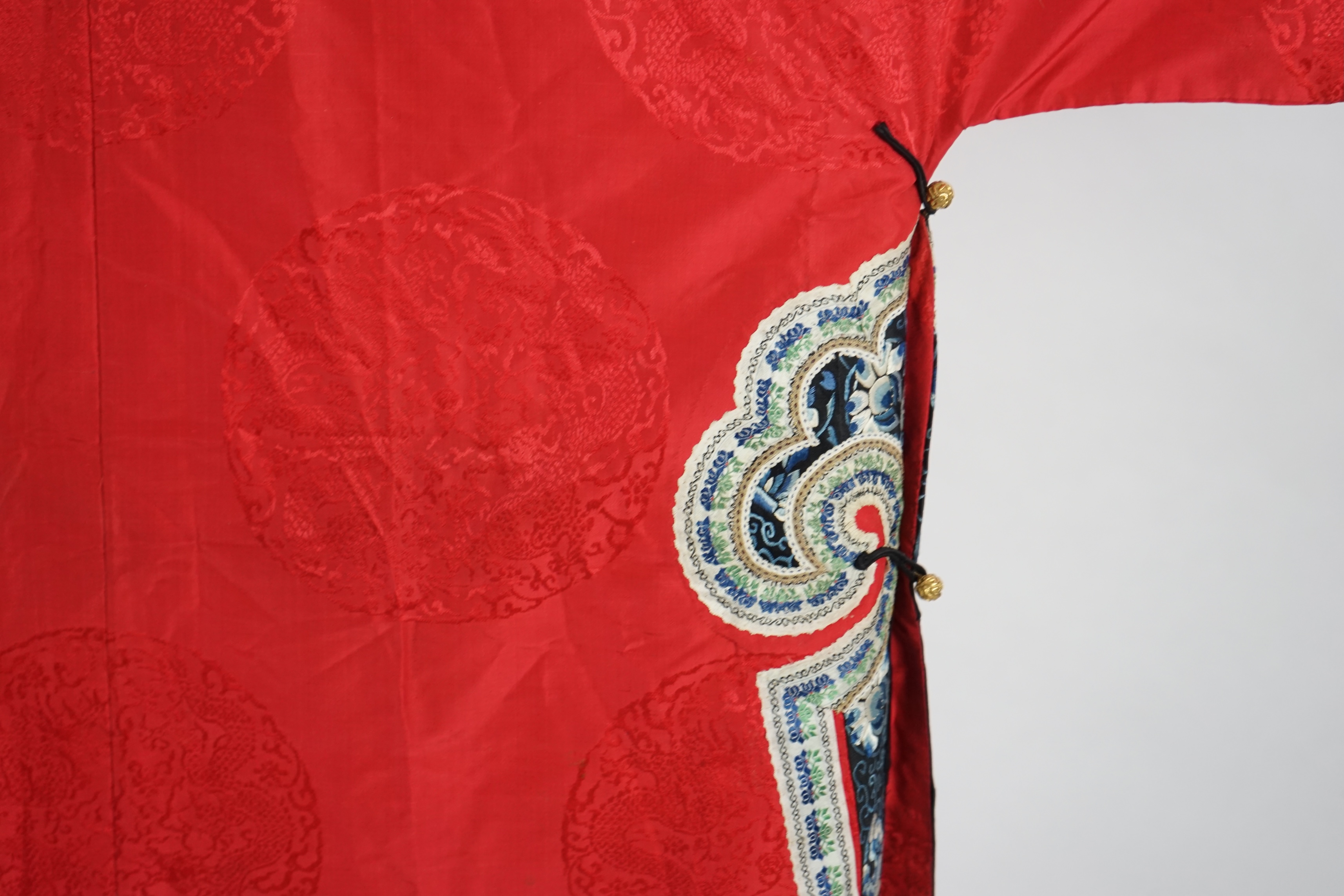 A late 19th century Chinese Manchu ladies red silk damask robe, with black and blue silk embroidered borders, ornately edged cream floral silk braiding, length from neck (back) to bottom edge 132cm long. Condition - stai